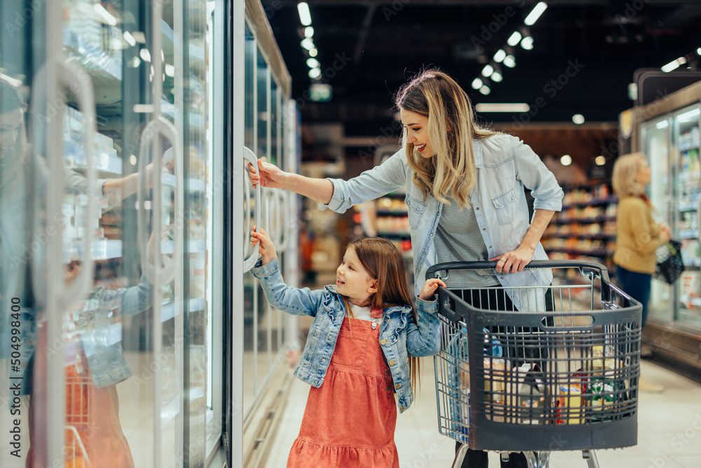Mother and daughter opening a beverage cooler together in a grocery store.