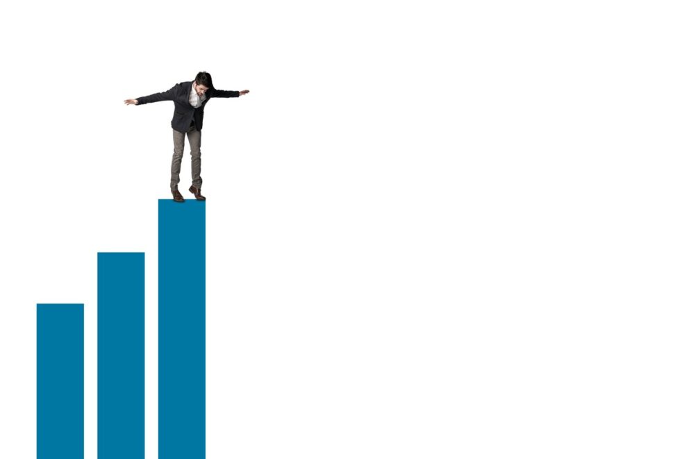 Business Person standing precariously atop a Bar Graph