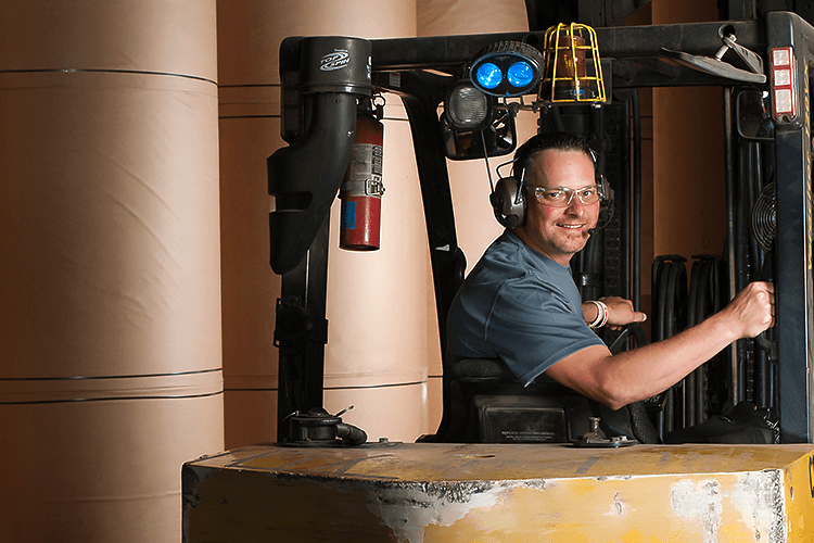 PCA Employee driving a forklift near rollstock in a box plant.